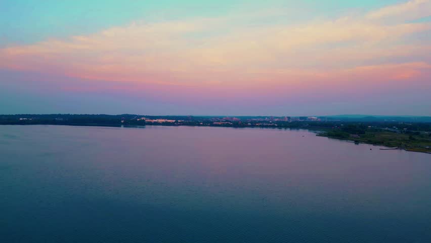 A descent down to the surface of the lake, capturing the city skyline in the distance and the surrounding landscape of the Central New York area as night approaches