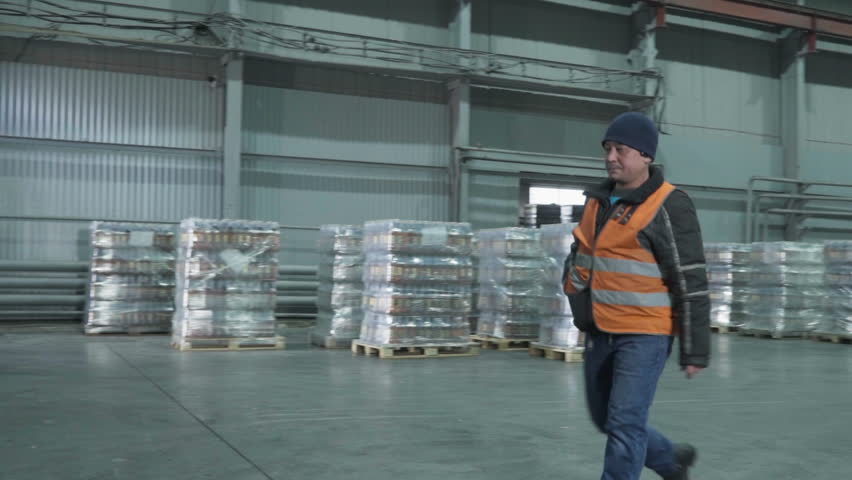 Workers on the trucks moving the shipment wares around the storage room. Workers transporting the wares inside of the factory storage. Workers carrying the storage supply wares at the plant.
