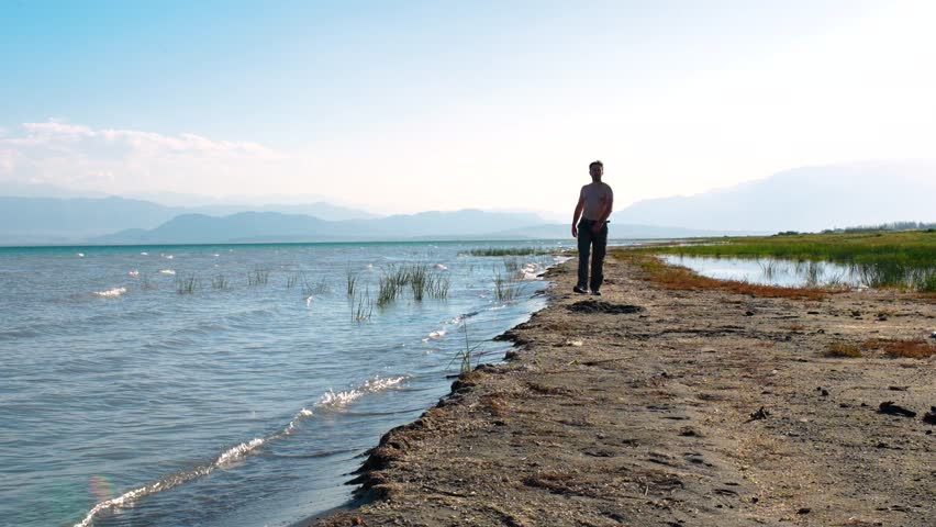 Shirtless man tourist walking on lake shore on summer day, vacation concept