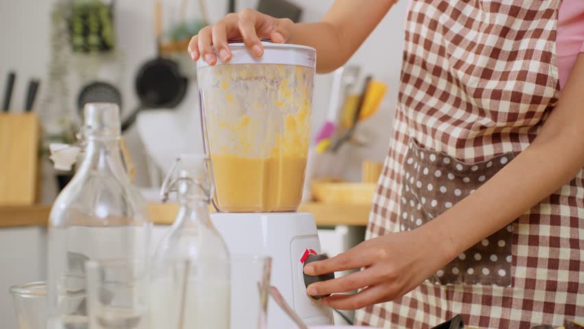 Close up of woman making fresh fruit smoothies in blender in kitchen. Attractive female housewife feel happy and relax, enjoy preparing ingredients and making healthy drink for breakfast in morning.