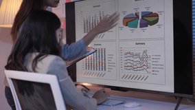 Two businesswomen analyze data on a large screen. Pointing at various charts and graphs, they engage in a discussion about the displayed information - Powered by Shutterstock - Get 15% off with code: PIKWIZARD15