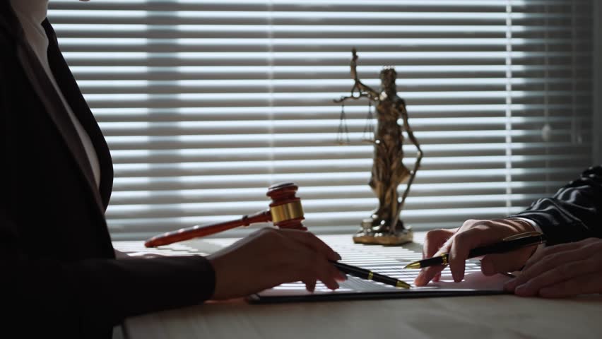Two lawyers in formal attire discussing contract specifics at a desk, with a prominent statue of lady justice in the background, highlighting the importance of legal proceedings