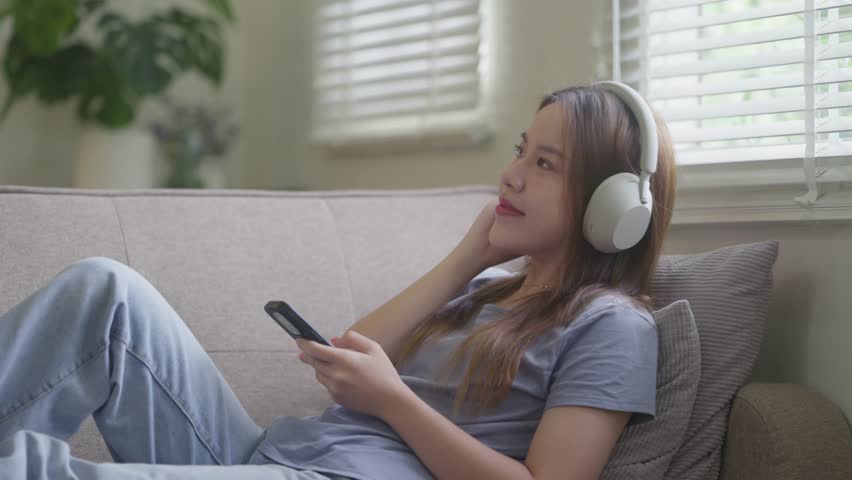 Asian woman wearing headphone listening music with her smartphone at home