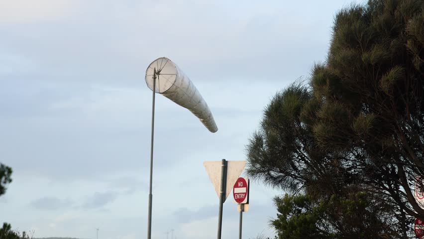 Windsock swaying near trees and road signs