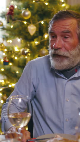 Happy old grandfather telling funny joke to his family gathering at table laughing together and enjoying Christmas dinner.