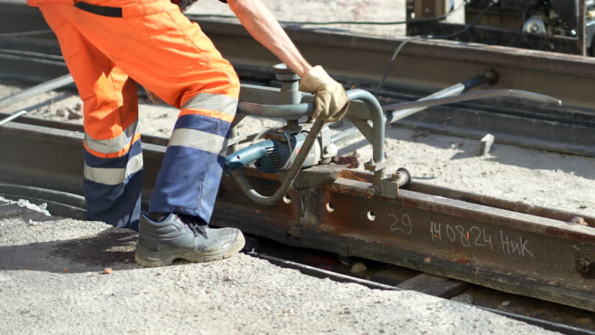 Unrecognizable worker grinding rail track after welding, sparks flying. Major tramway repairs, heavy physical labor, urban renovations, infrastructure improvement, public transportation maintenance
