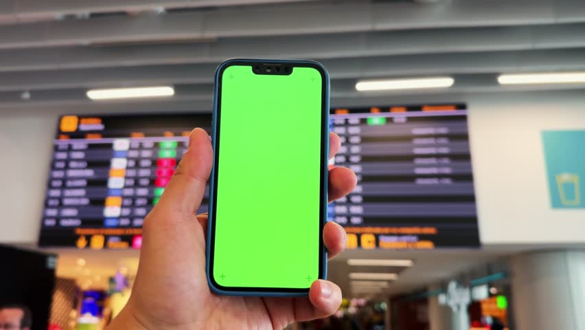 Tourist checking schedule table at the airport terminal and using phone application. Hands with green screen. Close-up technology concept.