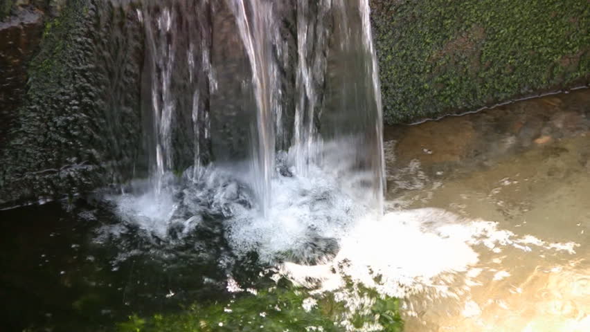 Water falls from the concrete, overgrown algae stage in a big pond