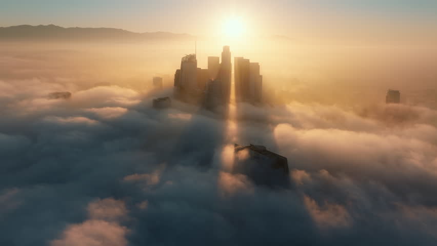 A breathtaking aerial shot beautifully captures the skyline of Downtown Los Angeles as it emerges gracefully from the morning fog, all while being bathed in the warm, golden sunlight of dawn