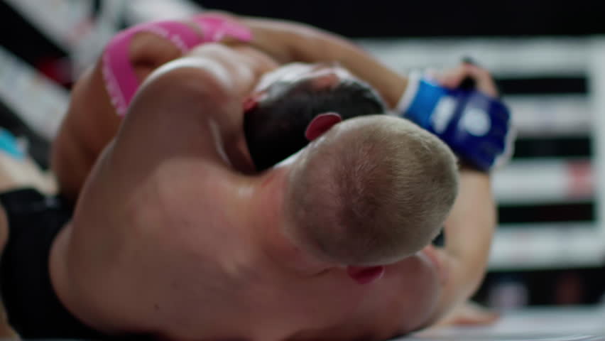 Two male athletes wrestling in a ring during a mixed martial arts championship. One fighter is wearing pink shorts and the other black shorts