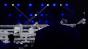 Businessman is sitting in a dark indoor stadium, watching a fighting championship. The stadium is lit with blue stage lighting - Powered by Shutterstock - Get 15% off with code: PIKWIZARD15