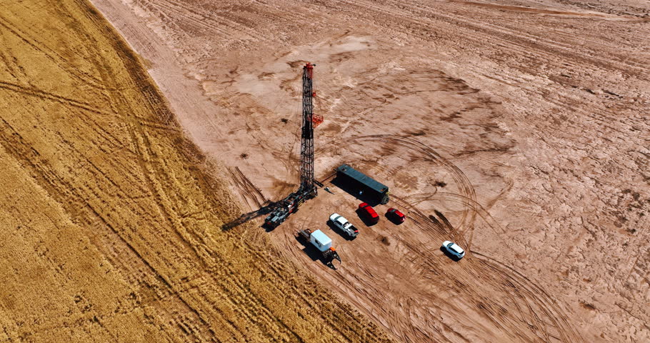Oil production site near the wheat field away from the big cities. Few cars stand at the derrick for drilling oil. Aerial view.