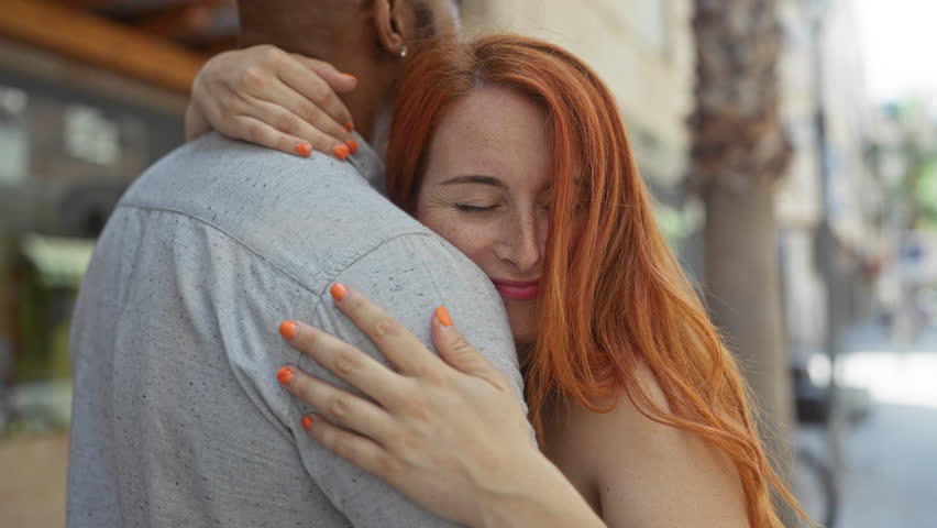 Interracial couple embracing and smiling on an urban street on a sunny day showcasing love, relationship, happiness, woman, man, outdoors, together, people, town, city