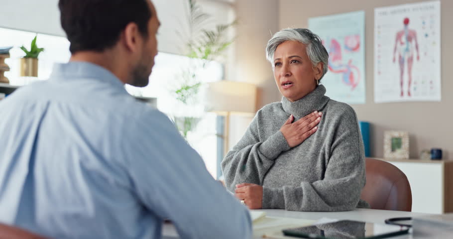 Chest pain, consultation and senior woman by doctor in hospital for reflux, heart attack or cough. Healthcare, discomfort and patient with medical worker for checkup with angina or cardiac disease.