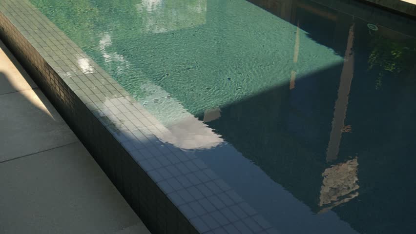 Orbit movement around the edge of a luxury private home swimming pool on a sunny day with ripples forming across the clear blue water