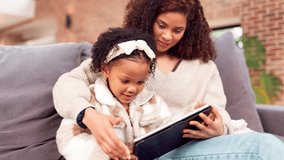 Education, remote learning on tablet and mother with daughter on sofa in living room of home together. Family, homework and smile of single parent woman with girl child in apartment for online study - Powered by Shutterstock - Get 15% off with code: PIKWIZARD15