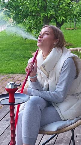 Woman smokes hookah on in backyard. Outdoor recreation with friends Vertical video. Taken from hand. High quality 4k footage