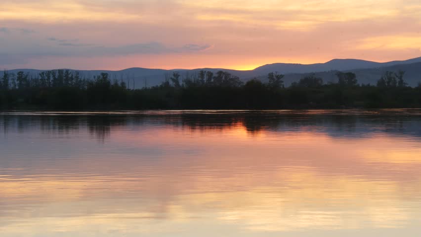 The sun has already set behind the horizon and now we are watching a beautiful picturesque sunset, which is reflected in the slow waters of the river on a clear autumn evening.

