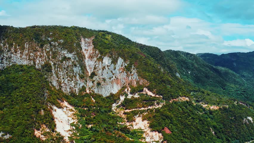 Picturesque highlands of the Dominican Republic on a sunny day. Colorful green slopes with rocky cliffs. Panoramic landscape of a mountain valley. Travel to a tropical paradise. Tourist destination.