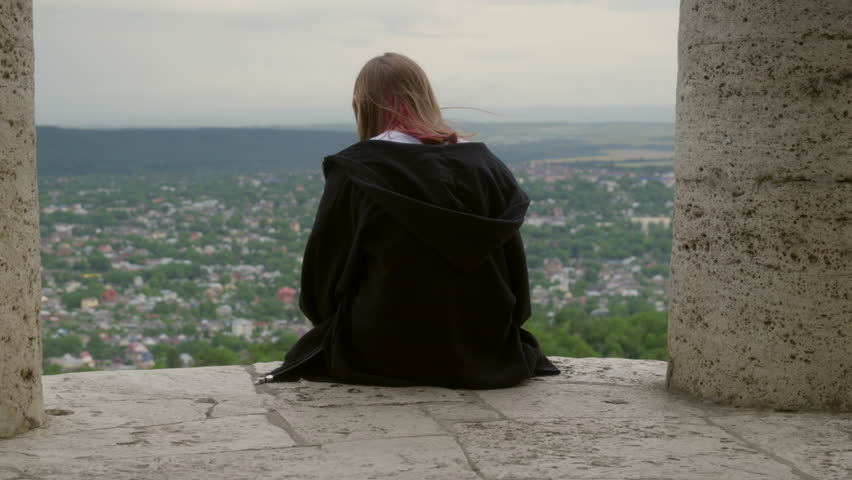 Back view Girl sitting on edge of stone rotunda and looking Internet Landscape. Woman reading mobile phone in park summer evening. Teen girl Swinging legs. Green park background. Browse internet