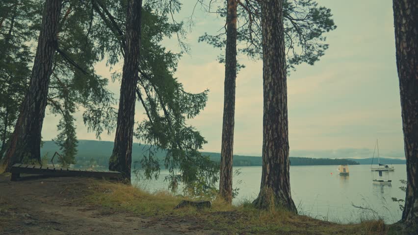 A place for relaxation and meditation. A path leading to a gazebo on the shore of a mountain lake. There are sailing boats on the lake.