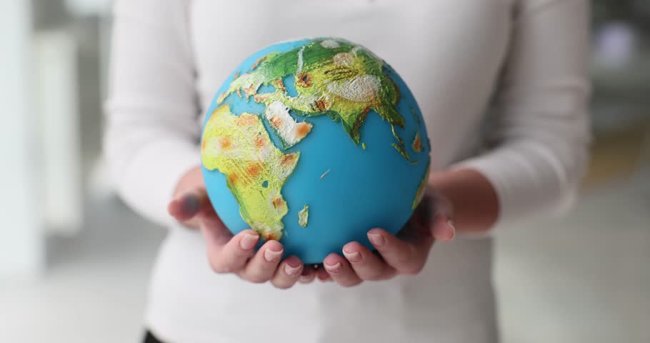 Woman holds miniature artificial model of Earth in hands. Female demonstrates vibrant continents and blue oceans on Earth globe showing vulnerability of planet
