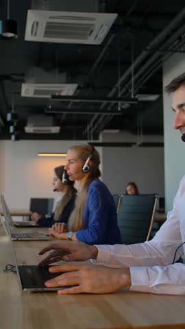 Attractive business person waring white formal shirt in office call center talking with client and then smile to camera. Concept of successful and cheerful solving of customer problems online