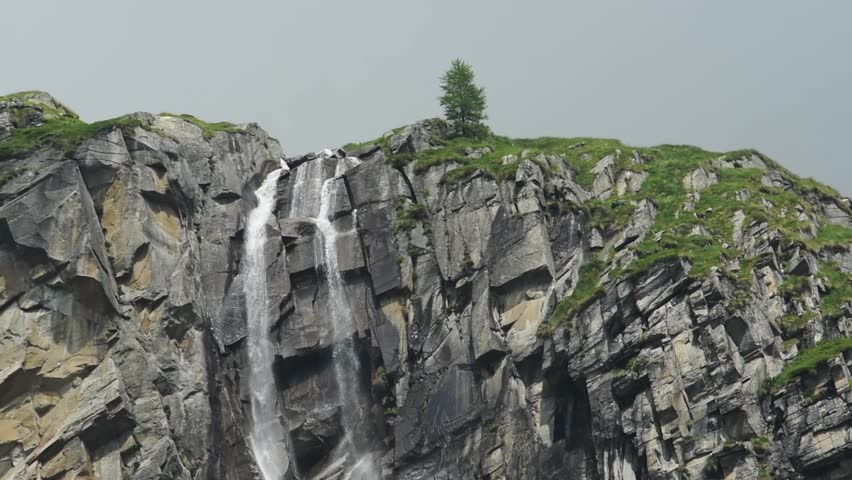 Rock waterfall off a cliff. Lone tree on the cliff. Alpine background