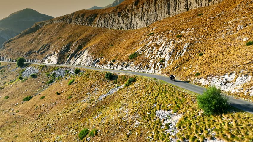 Fast sports motorcycle rides on mountain road with serpentines. Traveling together on motorbike concept. Summer adventure in the mountains. Aerial drone shot