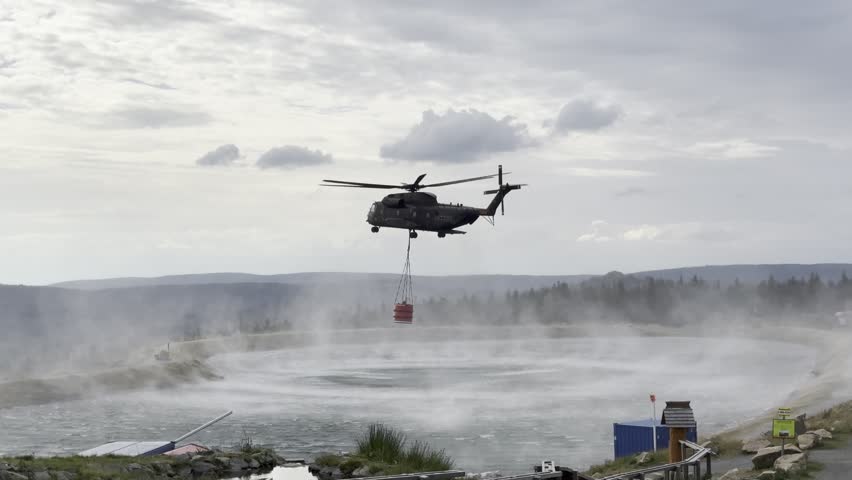 A CH-53 lifts off after filling a water bucket to fight a forest fire