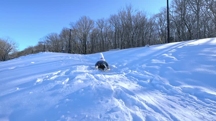Sledding in winter park, snow weather. Children ski in the winter with a slide on the tubing. Kid sledding down by the tube. winter leisure. Child climbing the slide to roll down it.