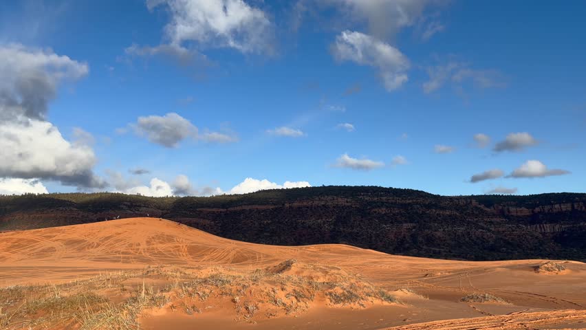 People enjoying their time sledding down the enormous and stunning sand dunes on a beautiful day at Coral Pink Sand Dunes State Park in Utah, USA.