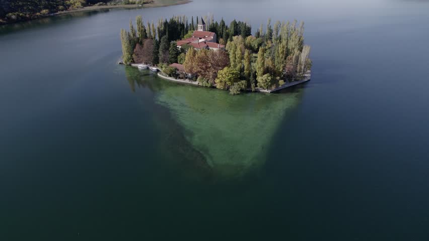 Aerial view of monastery island on serene lake surrounded by mountains, Visovac, Croatia.