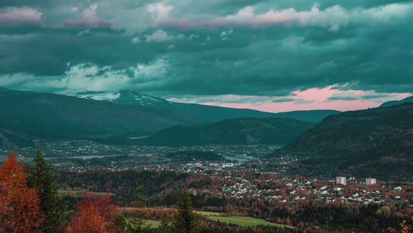 A panoramic view of a small town nestled in a mountainous valley, with dark, stormy clouds overhead. A timelapse video.