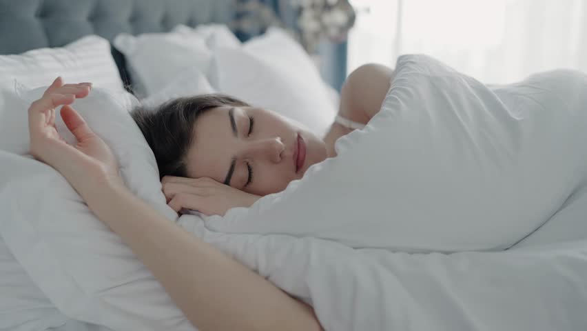 Young woman enjoying a restful sleep in a cozy bed wrapped in a white blanket, creating a sense of tranquility and relaxation. Perfect image for concepts of rest and relaxation. Young Woman Sleeping