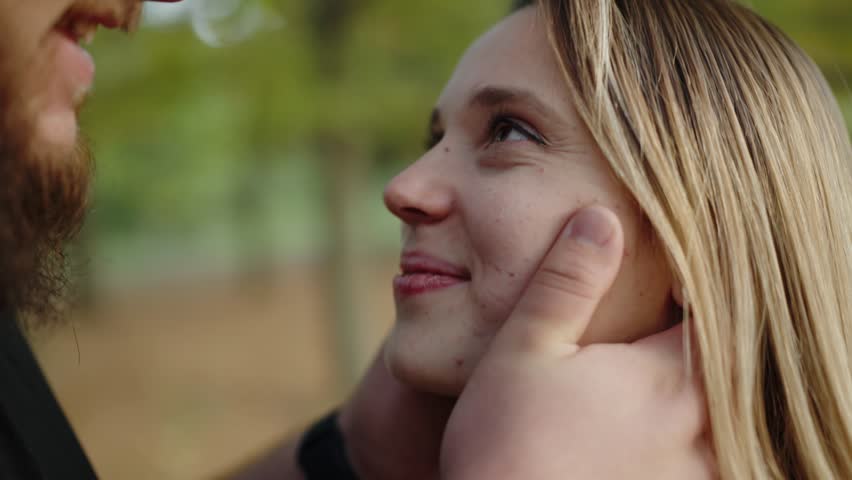 Close-up of a young woman smiling lovingly as her partner caresses her face gently, set against a blurred autumnal backdrop, symbolizing love and affection. Romantic Couple Enjoying A Tender Moment