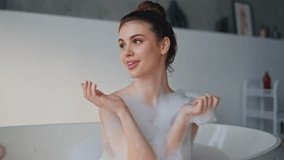 Bathing woman blowing kiss in luxury bathroom closeup. Joyful woman sitting in white foam home bathtub feeling happy. Playful beautiful brunette enjoying bodycare morning routine in bubble bath.  - Powered by Shutterstock - Get 15% off with code: PIKWIZARD15