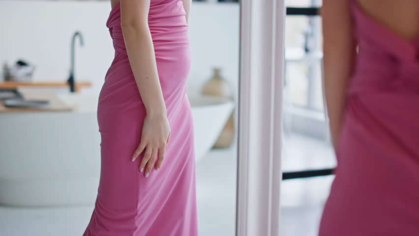 Woman enjoying new dress admiring reflection in modern bathroom closeup. Cheerful lady spinning around looking home mirror wearing elegant pink gown. Happy girl model posing choosing outfit for date.
