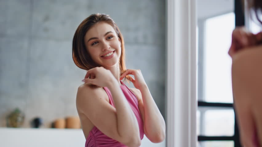 Woman enjoying new dress admiring reflection in modern bathroom closeup. Cheerful lady spinning around looking home mirror wearing elegant pink gown. Happy girl model posing choosing outfit for date.