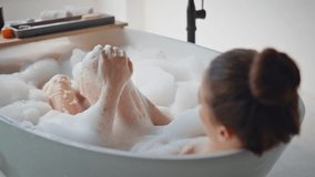 Girl cleansing legs with foam enjoying morning bodycare routine closeup. Relaxed woman bathing with white bubbles in luxury bathtub. Serene lady soaking in bath with calm expression. Self care concept - Powered by Shutterstock - Get 15% off with code: PIKWIZARD15