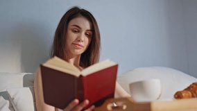 Morning girl reading novel having breakfast in bed closeup. Happy woman immersed in book drinking aromatic coffee on cozy bedding. Serene brunette enjoying calm literature hobby in light home bedroom. - Powered by Shutterstock - Get 15% off with code: PIKWIZARD15