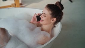 Bathing girl talking smartphone soaking in fluffy bubbles closeup. Cheerful woman calling boyfriend lying in luxury bathtub with foam. Relaxed smiling lady enjoy bath self-care with phone conversation - Powered by Shutterstock - Get 15% off with code: PIKWIZARD15