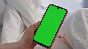 Hand holding mockup smartphone in bed calm morning closeup. Unknown woman relaxing on white bedding browsing green screen cellphone. Relaxed lady watching chroma key mobile phone in light bedroom. - Powered by Shutterstock - Get 15% off with code: PIKWIZARD15