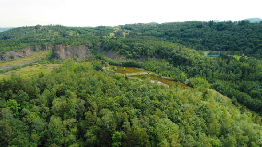 Lush forest clings to rocky outcrops in a breathtaking natural landscape, bathed in sunlight. Aerial view of river and green nature. Majestic rocky formations stand tall amidst greenery.