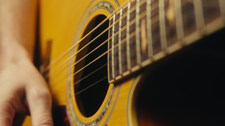 Young musician man sitting and playing acoustic guitar among music equipment in studio close-up. Guitarist plays melody 