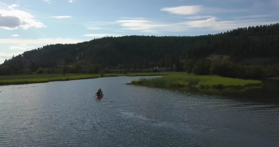 Two men row a canoe through shallow marshland in Lake Coeur d