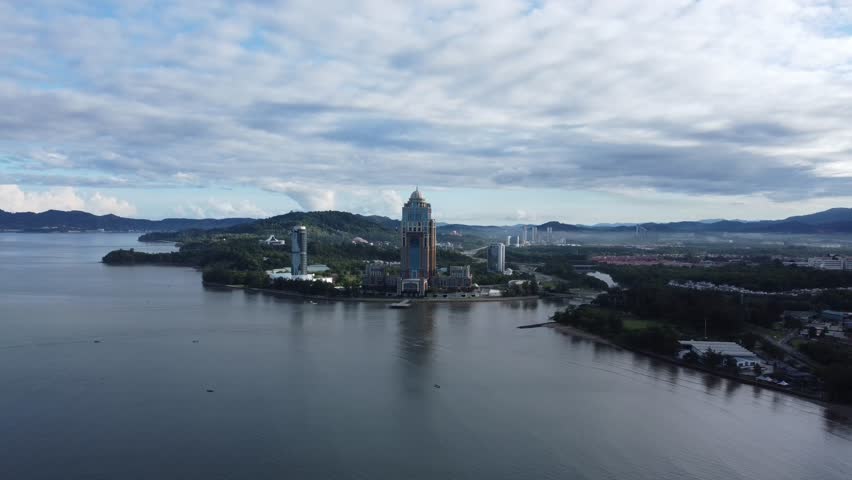 Drone shot focusing on tall landmark building in Kota Kinabalu, Malaysia. Morning clouds and large valleys can be seen beyond the horizon.