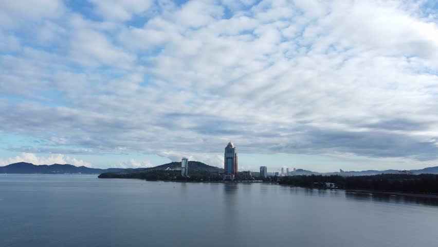 Drone slowly rises up as it flies toward beautiful tall landmark building across the ocean, during morning of Kota Kinabalu, Malaysia