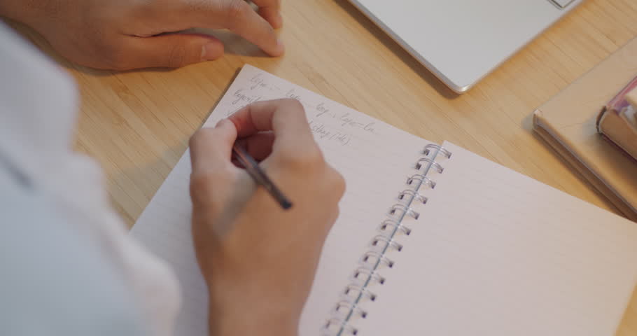 Close-up top view of male hand writing equation in notebook while teenager studying algebra doing homework at table. Education and knowledge concept.