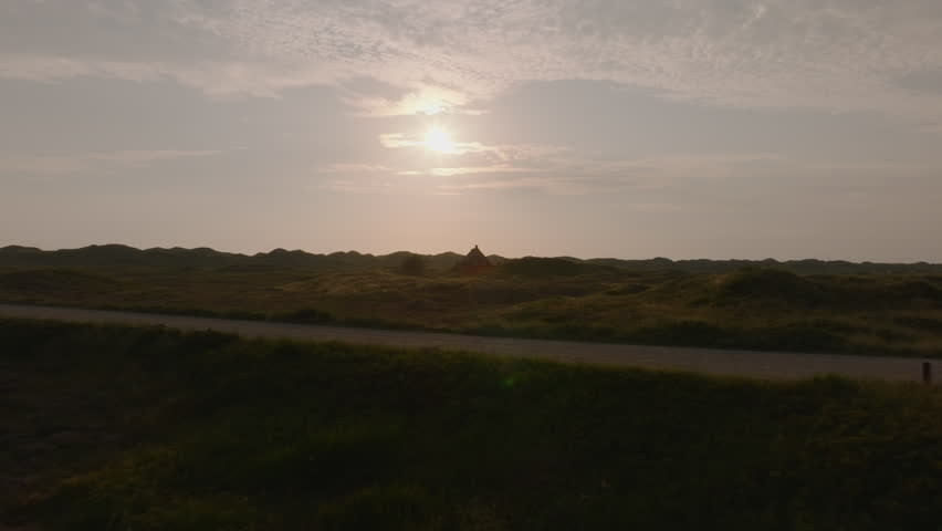 Sunlight bathing a lone building in the Ringkobing Fjord landscape during sunset highlights Denmark